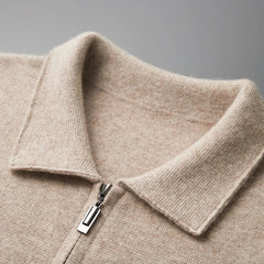 Close-up of a beige merino wool zip-up sweater with a folded collar and silver zipper, offering natural temperature regulation, shown against a plain gray background.