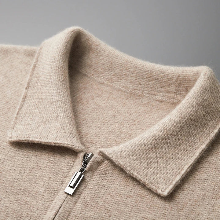Close-up of a beige merino wool zip-up sweater with a folded collar and silver zipper, offering natural temperature regulation, shown against a plain gray background.
