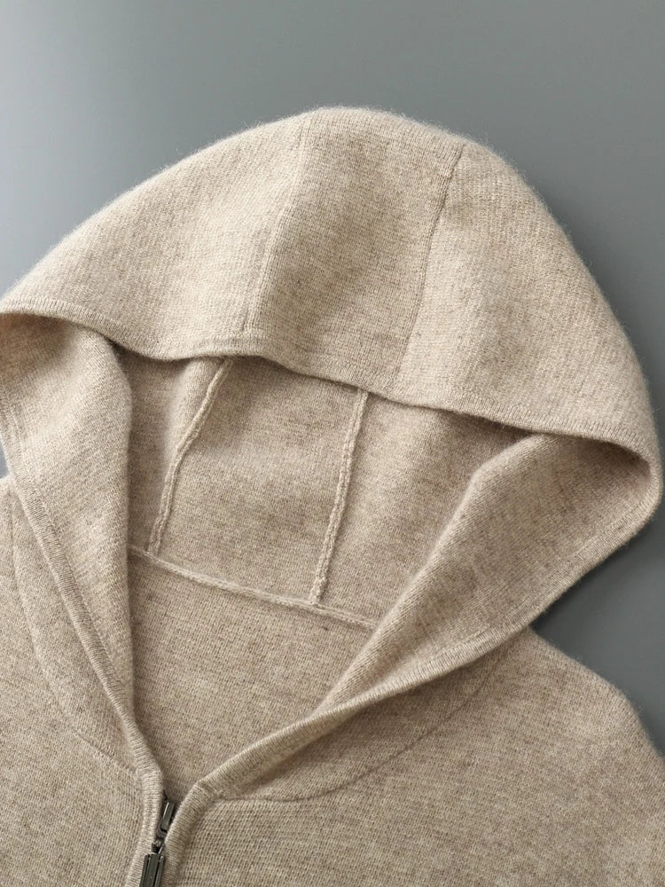 A close-up of a beige, soft-textured autumn winter sweater laid flat, showing the hood and part of the zipper front on a gray background.
