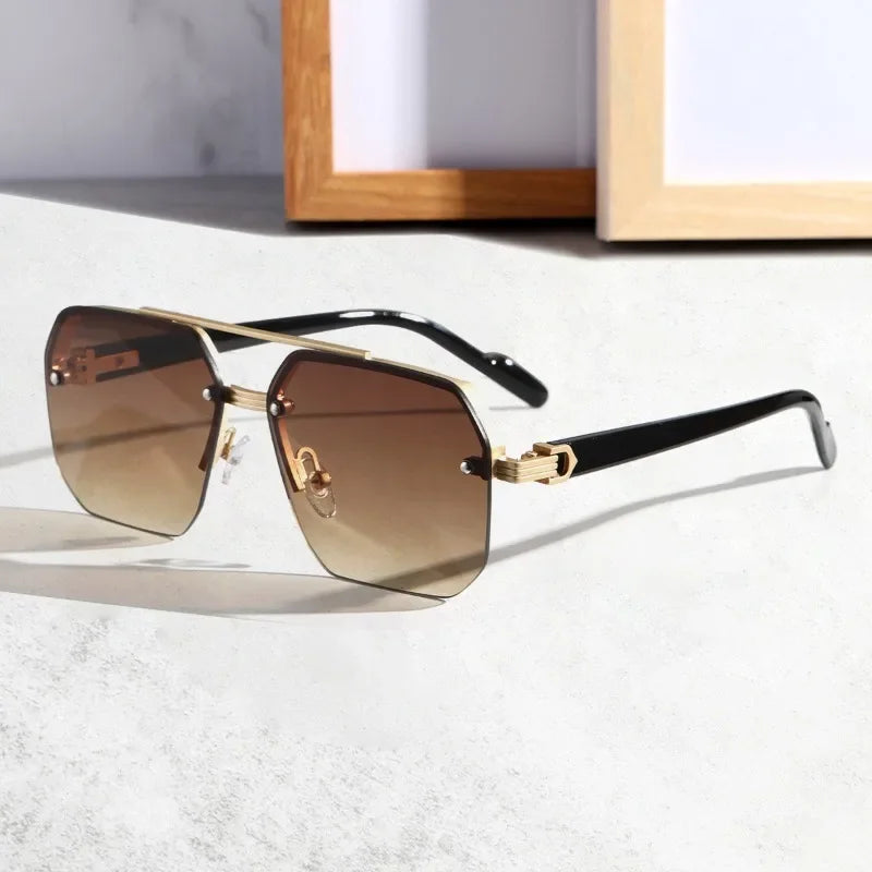 A pair of stylish sunglasses with UV400 protective lenses, gradient brown tint, a gold geometric metal frame, and black arms resting on a light surface, with picture frames blurred in the background.
