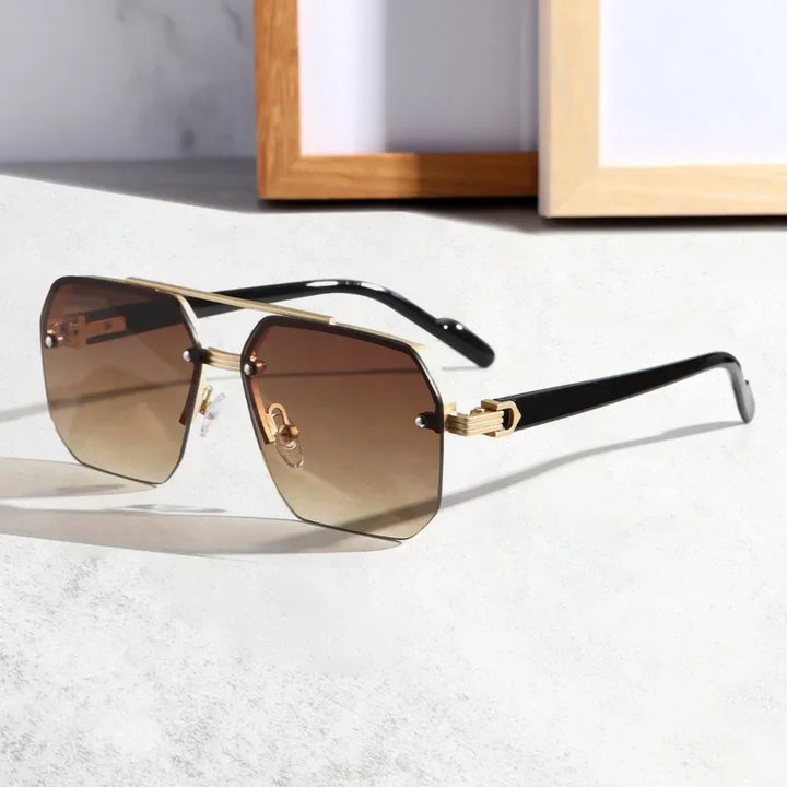 A pair of stylish sunglasses with UV400 protective lenses, gradient brown tint, a gold geometric metal frame, and black arms resting on a light surface, with picture frames blurred in the background.