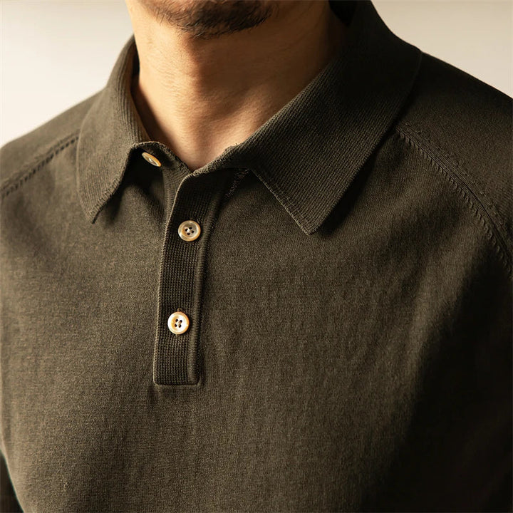 A close-up of a person wearing a classic style polo in dark olive green with a collar and three beige buttons, showing part of the chin and neck but not the full face.