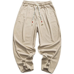 Beige, loose-fitting cotton blend sweatpants with a drawstring waistband for an adjustable fit, ribbed texture, white text drawstring, and knotted cuffs at the ankles, laid flat on a white background.