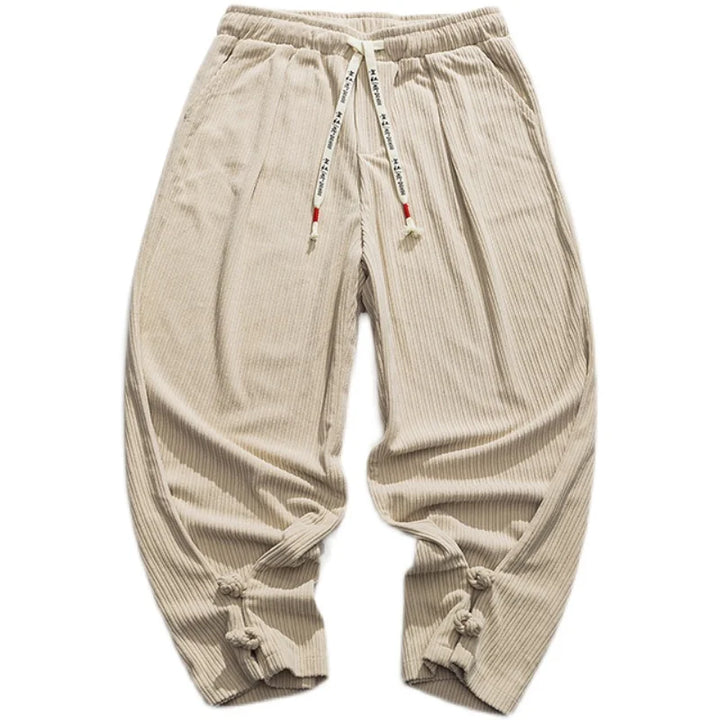 Beige, loose-fitting cotton blend sweatpants with a drawstring waistband for an adjustable fit, ribbed texture, white text drawstring, and knotted cuffs at the ankles, laid flat on a white background.