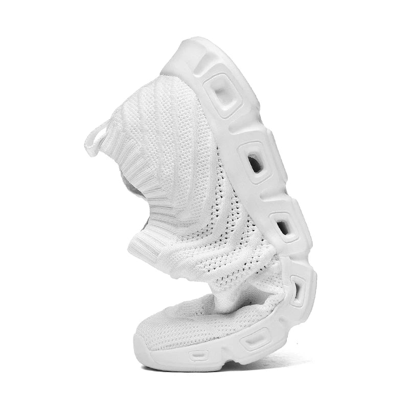 A white athletic shoe with a flexible, thick cushioned sole is bent in half, showcasing its softness and flexibility. The knit upper provides a sock-like fit, while multiple cutouts in the sole enhance movement.