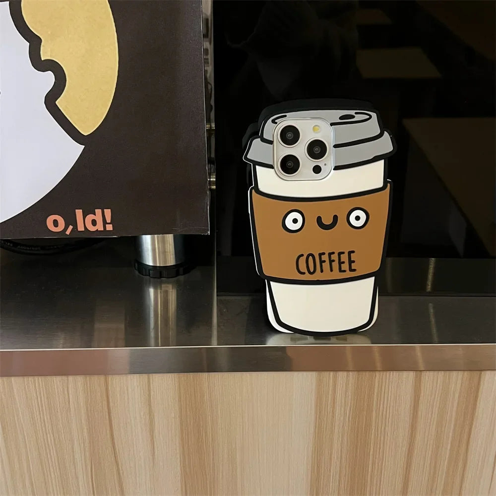 A phone with a 3D coffee cup soft silicone case sits on a counter next to a sign with part of a yellow and white design and the text o,Id! partially visible.