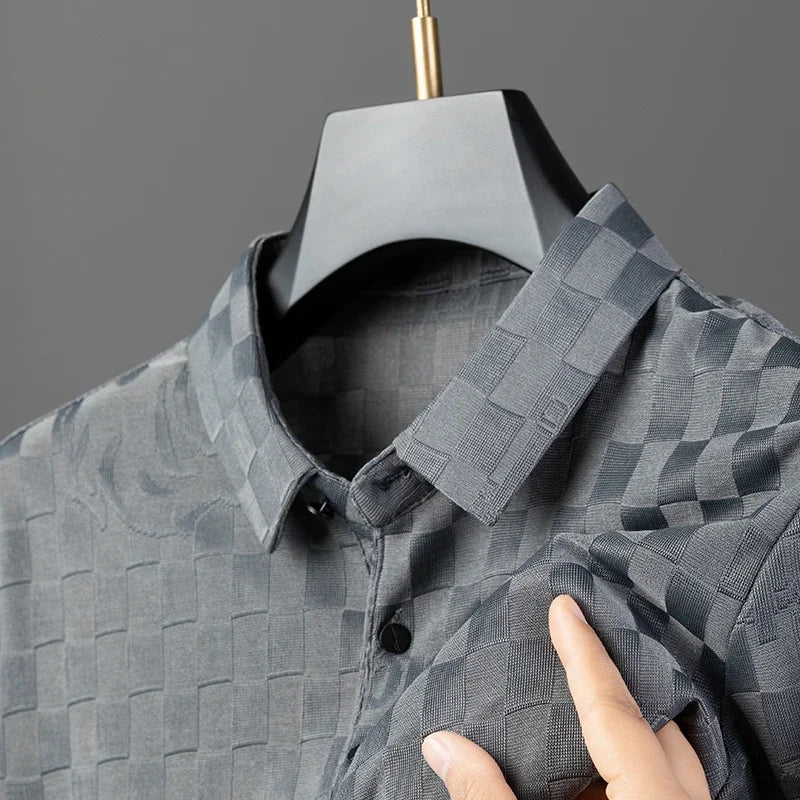 A close-up of a gray, checkerboard pattern button-up shirt on a black hanger, with a hand gently holding the fabric to show its texture and design against a plain gray background.