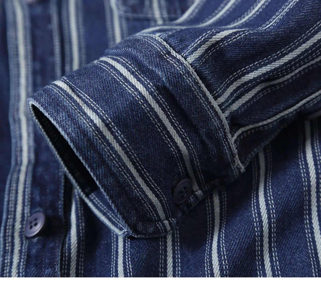 A close-up of the cuff and sleeve of a blue denim vintage button-up shirt with white vertical stripes, dark buttons, and a relaxed fit.