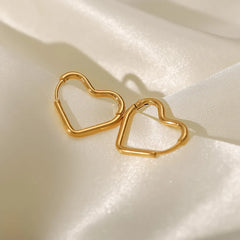 Two gold heart-shaped hoop earrings, known as the Eternal Love Earrings, rest on smooth, cream-colored satin fabric, catching the light and casting soft shadows—a perfect example of elegant craftsmanship.