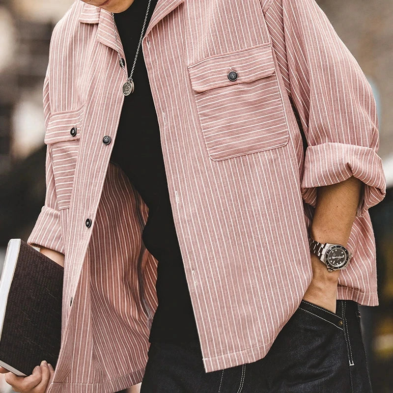 A person wearing a light pink and white pinstripe shirt with rolled-up sleeves, black shirt underneath, a watch on their wrist, and holding a closed notebook. Only the torso is visible.