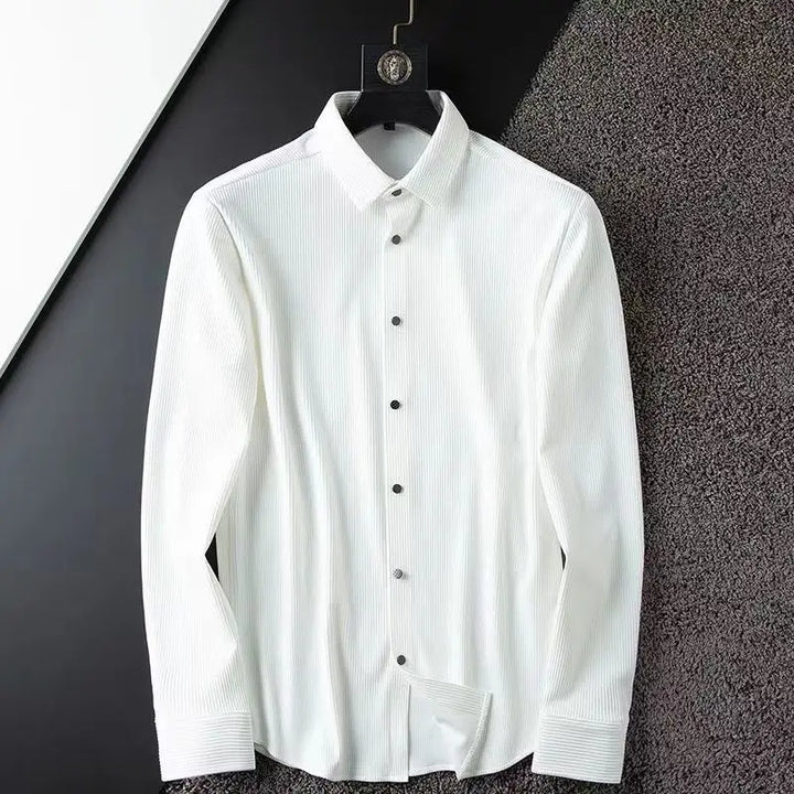 A white, long-sleeved button-up shirt with thin vertical stripes, made from ultra soft fabric, hangs on a black hanger against a textured, two-tone black and gray wall.