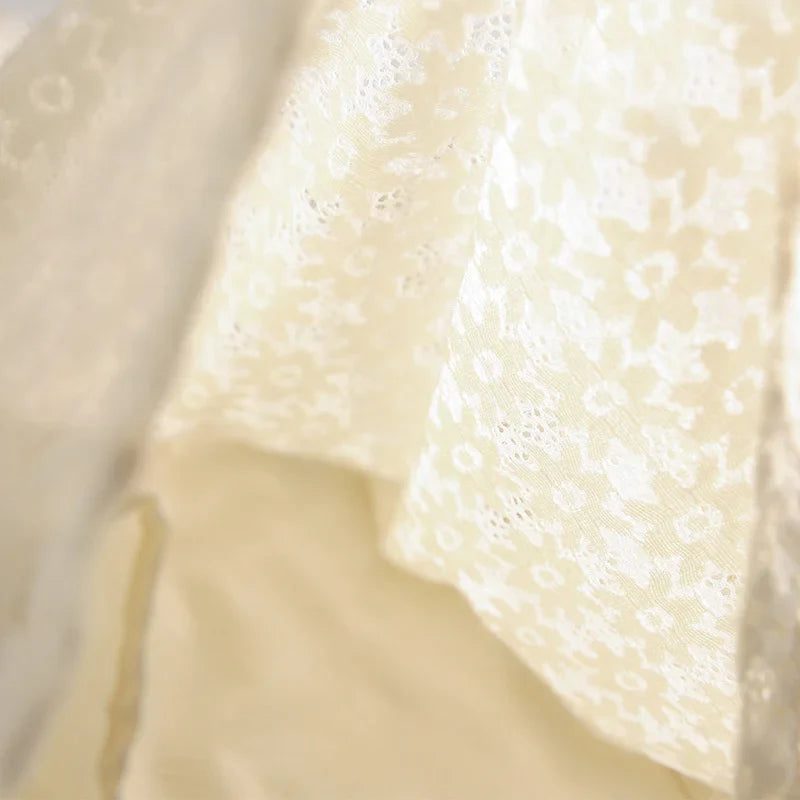 Close-up of an ivory lace blouse featuring a delicate floral lace pattern, softly draped and illuminated by gentle light, highlighting the intricate texture and details.