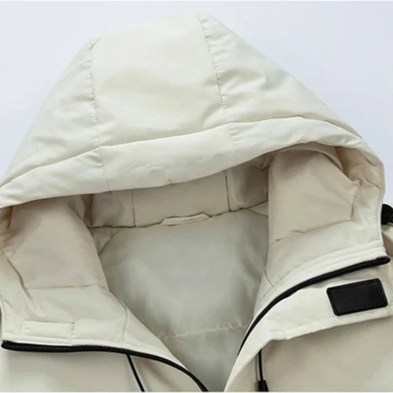 Close-up of a light beige hooded jacket, featuring a windproof, padded fabric and showing the hood and top of the zipper area with a black velcro strap detail on one side. The material appears soft and insulated.