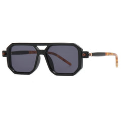 Geometric black sunglasses with dark lenses and thick, angular frames. This luxury eyewear features temples that are black near the hinges and transition to a light tortoiseshell pattern toward the ends.