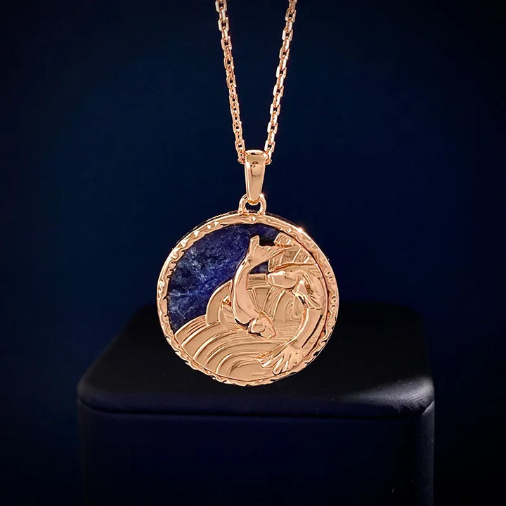 A gold zodiac necklace featuring a circular design with an intricately detailed fish jumping out of stylized waves, set against a deep blue background. The pendant hangs from a delicate gold chain, perfect for astrology jewelry lovers.