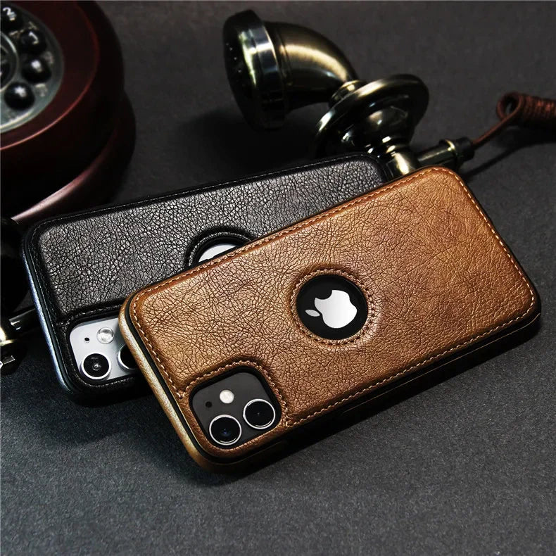 Two smartphones with luxury leather phone cases—one brown, one black—rest on a dark surface near an old-fashioned rotary telephone handset. The Apple logo is visible through circular cutouts, highlighting their slim protective case design.