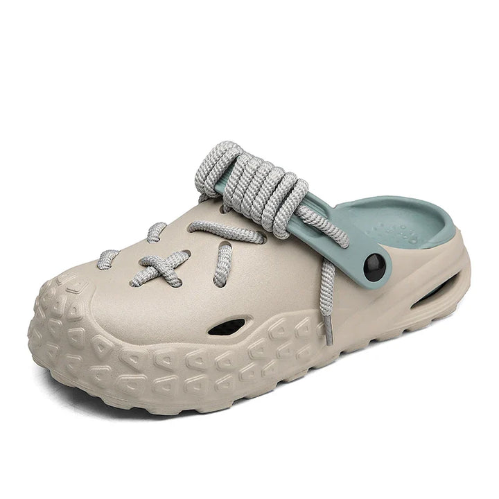 A beige slip-on clog with a textured sole for enhanced grip, gray rope lace detail, and a light blue adjustable heel strap. The design mimics sneaker laces and has a rugged, chunky appearance.