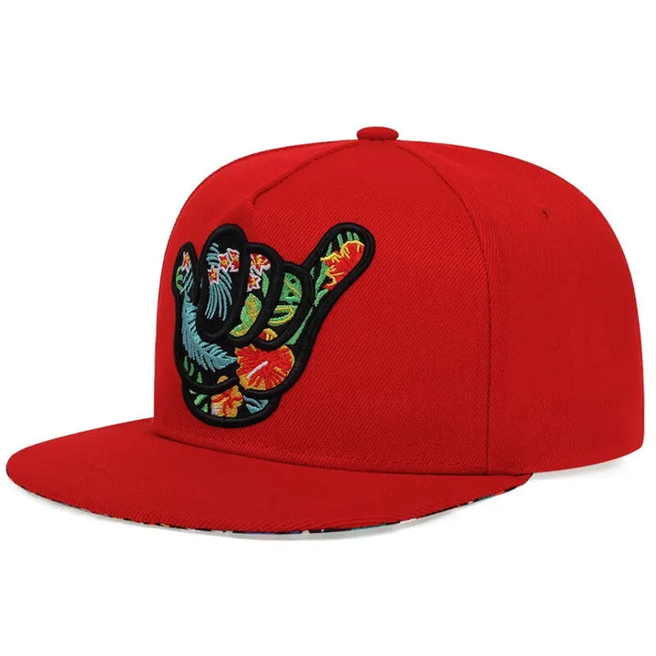A bright red tropical snapback featuring a colorful embroidered shaka hand sign with a tropical floral pattern on the front.