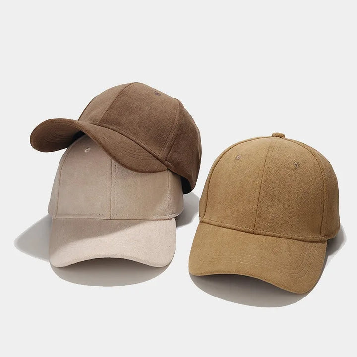 Two suede baseball caps are shown on a white background. These unisex streetwear caps come in brown and tan, each featuring a classic six-panel design—the brown cap rests at an angle atop the upright tan cap for a retro touch.