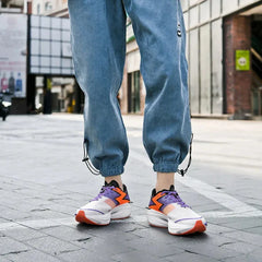 Person standing on a city street wearing light blue jogger pants and colorful sneakers with a shock-absorbing sole. The shot is focused on their legs and shoes with buildings in the background.