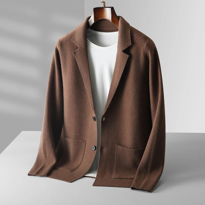 A brown, two-button blazer with front pockets is draped over a hanger, layered atop a plain white t-shirt—an ideal pairing with a men's wool cardigan for an effortlessly refined look against a neutral, softly lit background.