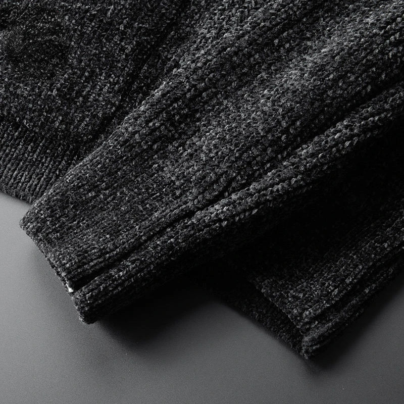 Close-up of the sleeve and body of a dark textured knit sweater, crafted from a soft cashmere wool blend, laid on a flat, smooth surface. The fabric appears thick with a visible, slightly fuzzy pattern—perfect for layering.
