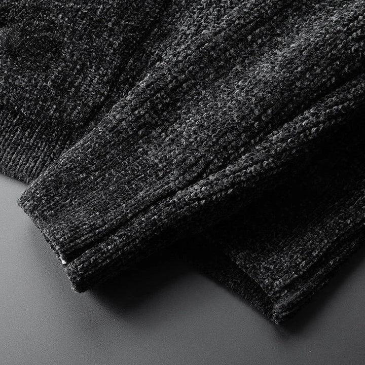 Close-up of the sleeve and body of a dark textured knit sweater, crafted from a soft cashmere wool blend, laid on a flat, smooth surface. The fabric appears thick with a visible, slightly fuzzy pattern—perfect for layering.