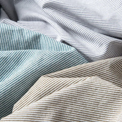 Close-up of several pieces of fabric with diagonal pinstripes in light blue, gray, beige, and off-white, reminiscent of a classic pinstripe shirt, draped and overlapping each other.