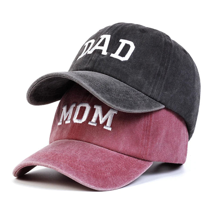 Two baseball caps stacked together—one black embroidered cap with DAD in white, and one pink with MOM in white—perfect as a vintage streetwear Mom & Dad cap set.