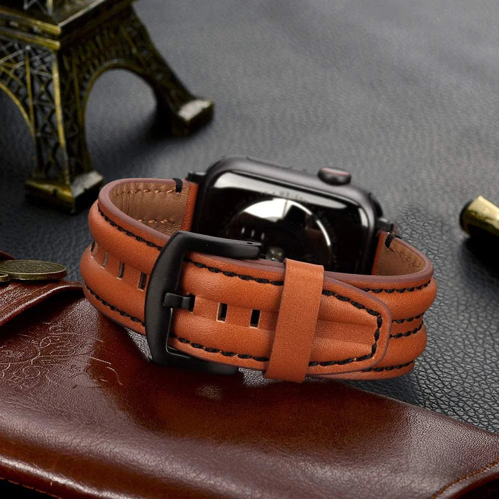 A brown leather Apple Watch strap with black stitching is attached to a smartwatch, resting on a leather surface beside a miniature Eiffel Tower and a brown wallet.