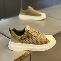 A stylish olive-green woven upper sneaker with a cushioned sole and matching laces is displayed on a reflective surface; another similar shoe is blurred in the background.