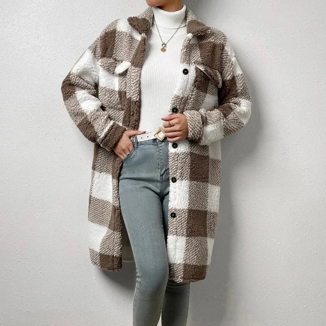 A person stands against a plain wall wearing a plaid Sherpa coat in brown and white with an open lapel over a white turtleneck sweater and light gray jeans. The cozy coat features large checks, black buttons, and a relaxed loose fit.