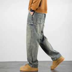 A person wearing a brown sweatshirt, classic denim stone washed straight leg jeans with side pockets, and tan sneakers stands on a gray floor against a plain white background.