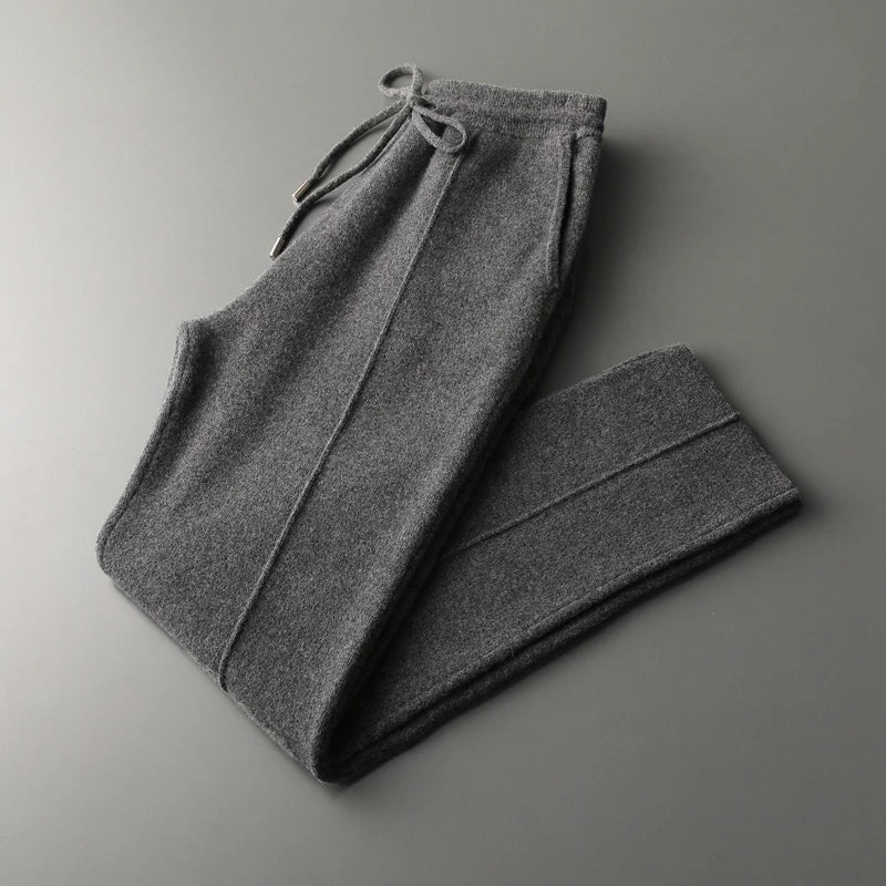 A pair of winter warm, dark gray cashmere wool blend sweatpants with a drawstring waistband, folded neatly on a smooth gray surface.