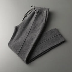 A pair of winter warm, dark gray cashmere wool blend sweatpants with a drawstring waistband, folded neatly on a smooth gray surface.