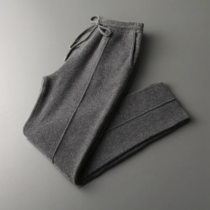A pair of winter warm, dark gray cashmere wool blend sweatpants with a drawstring waistband, folded neatly on a smooth gray surface.