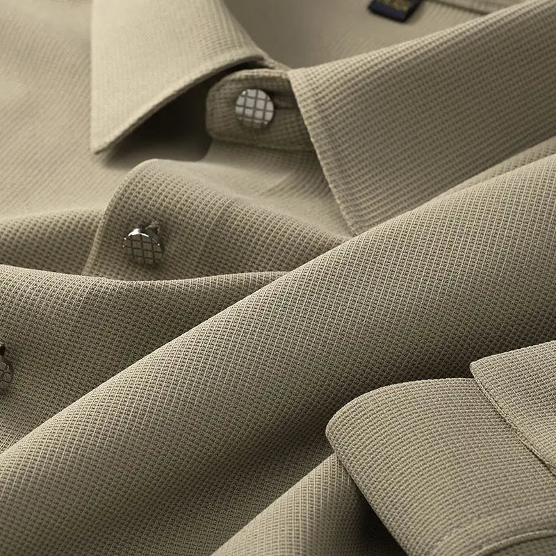 Close-up of a beige wrinkle-resistant shirt with a grid-like pattern, featuring metal buttons and visible collars and cuffs. The fabric appears smooth and finely woven.