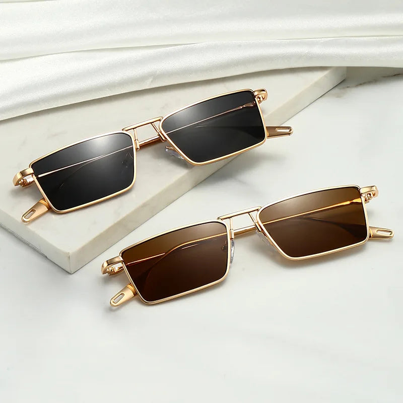 Two pairs of Avalon Sunglasses with gold frames and rectangular lenses—one with black and one with brown tints—are displayed on a marble surface, complemented by a white cloth in the background.