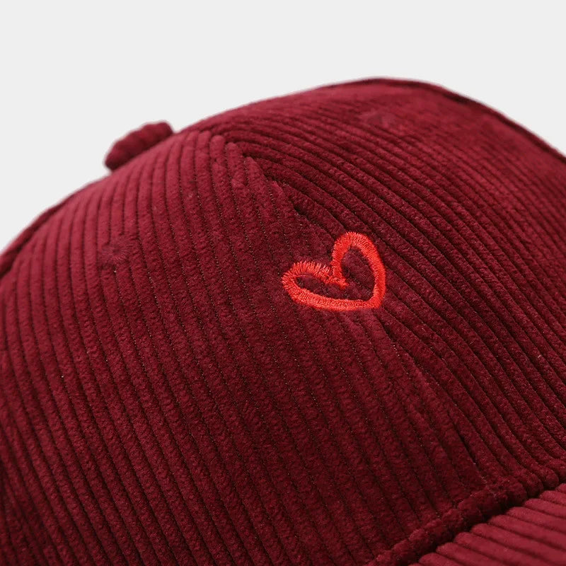 Close-up of a burgundy corduroy hat with a small red heart embroidery on the front and a comfortable FlexFit band for a perfect fit.