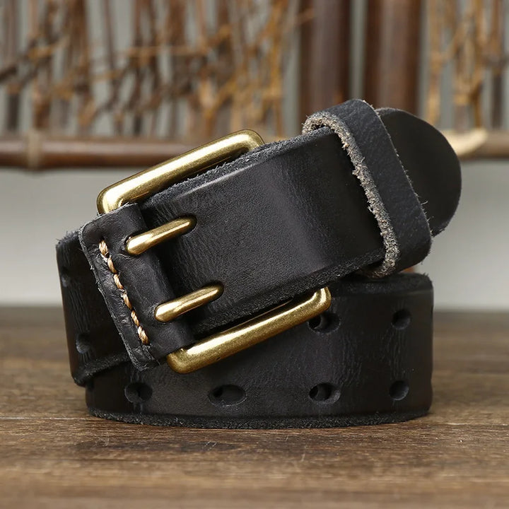 A rolled-up genuine leather belt with a gold double-prong buckle sits on a wooden surface, highlighting heritage craftsmanship against a blurred woven background.