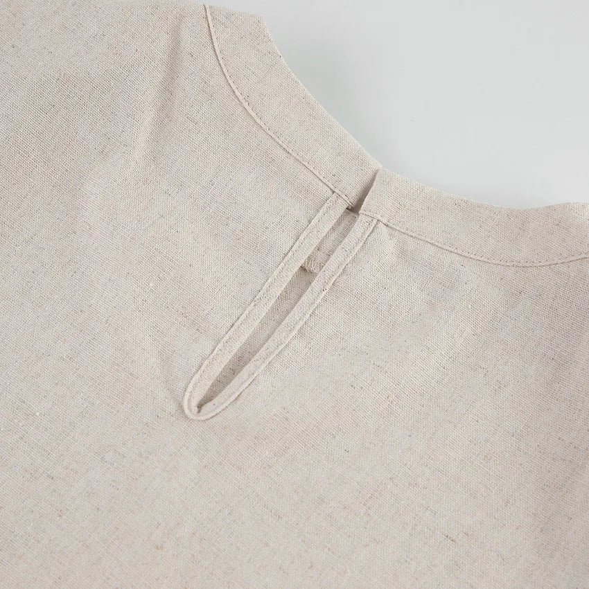 Close-up of the back neckline of a beige Belgian Linen Blend garment, showing a small vertical slit with a single fabric loop and button closure. The fabric has a natural, textured appearance.