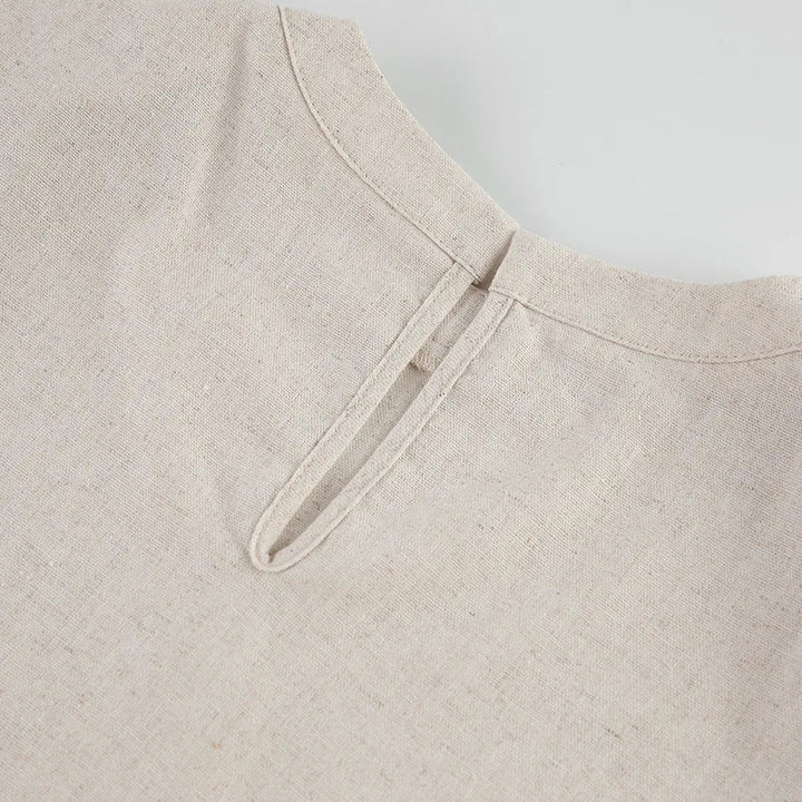 Close-up of the back neckline of a beige Belgian Linen Blend garment, showing a small vertical slit with a single fabric loop and button closure. The fabric has a natural, textured appearance.