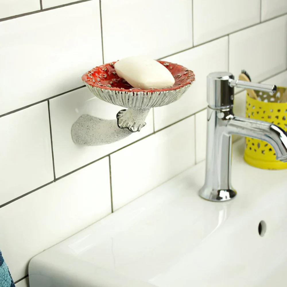 A decorative soap dish shaped like a hand holds a bar of soap above a white sink with a chrome faucet, against a white tiled wall. This unique home decor piece adds charm, with a yellow container and naturalistic design touches in the background.