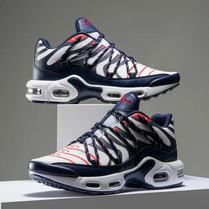 A pair of stylish athletic sneakers with white, navy blue, and red accents. Featuring a wavy black overlay design, breathable mesh upper, visible air cushions in the soles, and displayed against a plain gray background.