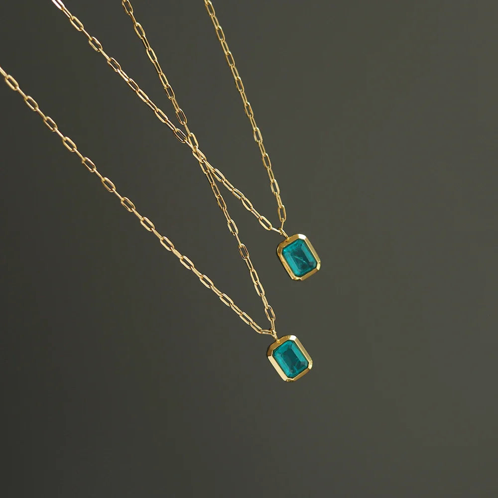 Two delicate 18K gold plated chains with rectangular green zirconia pendants are displayed against a plain dark background.