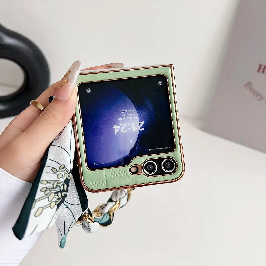 A hand with manicured nails and a floral scarf bracelet holds a Samsung Galaxy Z Flip in a premium leather case, showing its external screen with the time 21:24 and dual cameras.