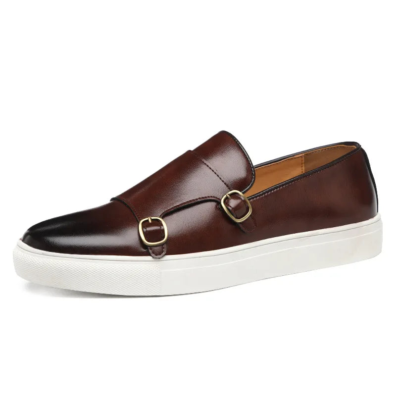 A brown leather slip-on loafer with double monk straps, gold buckles, and a white rubber sole embodies British fashion in men’s casual leather shoes, displayed on a white background.