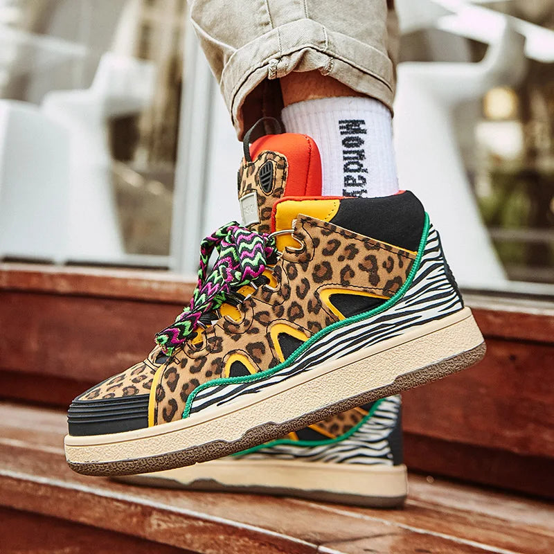 A person wearing lightweight animal print shoes with colorful laces, white socks, and rolled-up beige pants stands on wooden steps. The sneakers feature leopard, zebra, and cheetah patterns with green and orange accents.