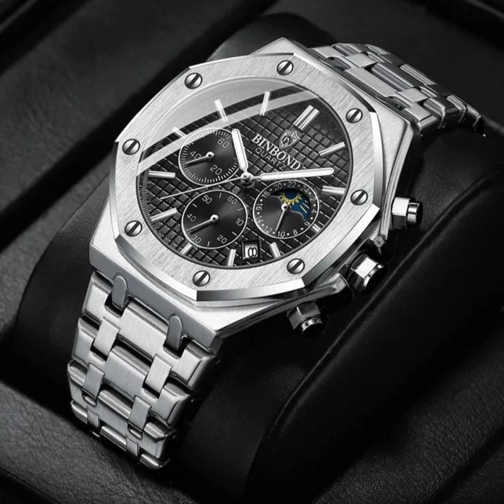 A luxury stainless steel watch with a textured black dial, three chronograph dials, and a metal link band, displayed on a black leather cushion. The BINBOND face highlights a moon phase indicator for added elegance.