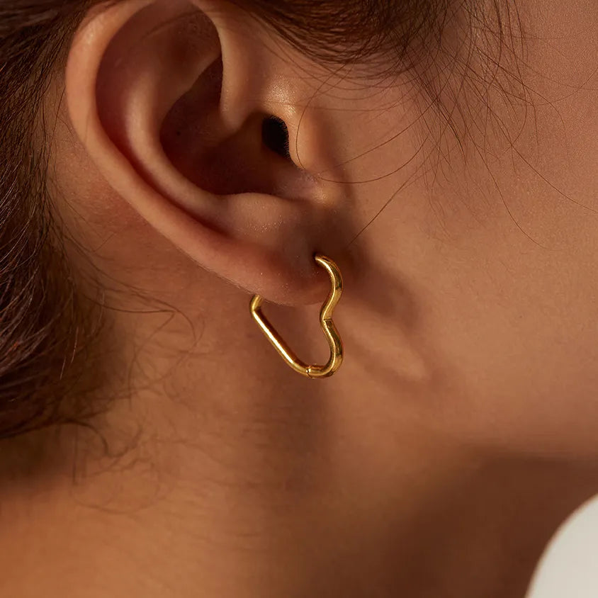 Close-up of a persons ear wearing the Eternal Love Earrings, featuring an abstract, irregular gold hoop. The persons hair is pulled back, revealing the elegant craftsmanship and minimalist design against their skin.